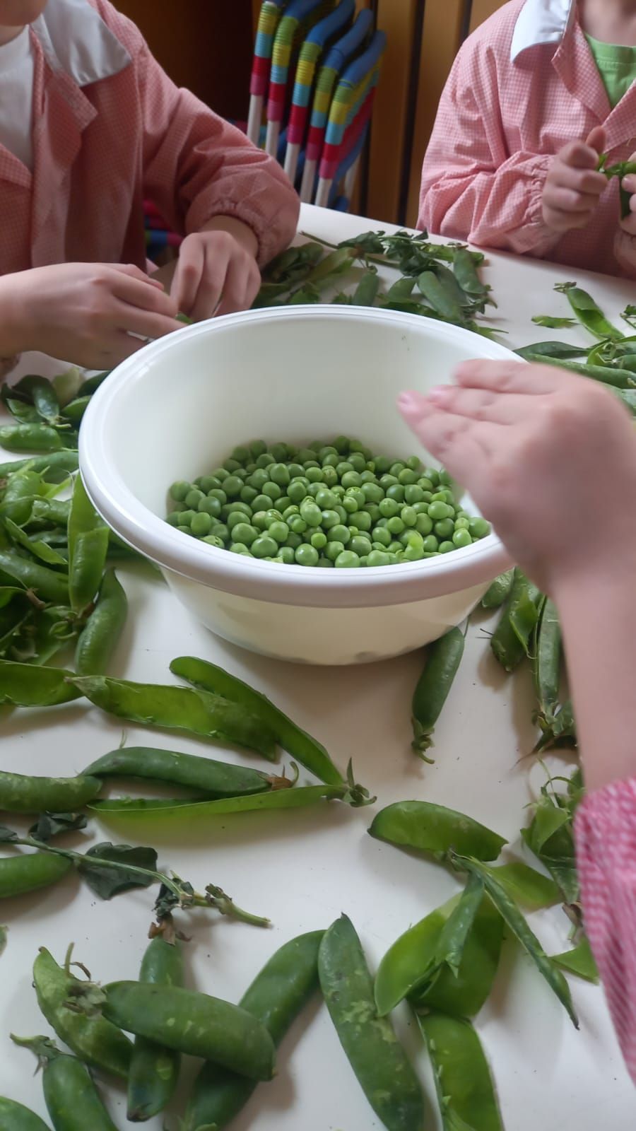 Una ciotola di piselli è circondata da piselli su un tavolo.