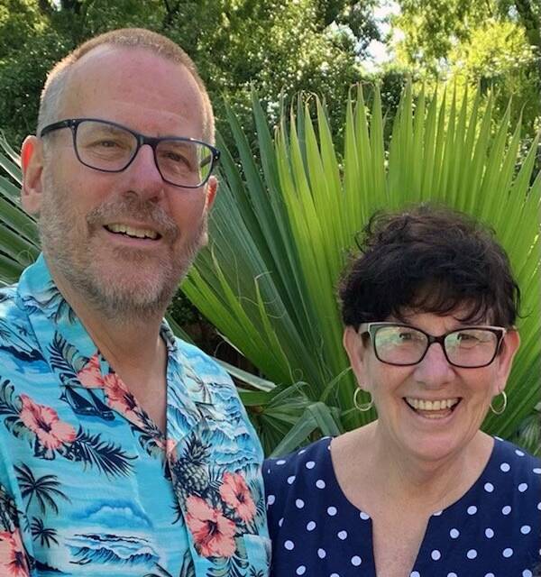 a man and a woman are posing for a picture in front of a palm tree .