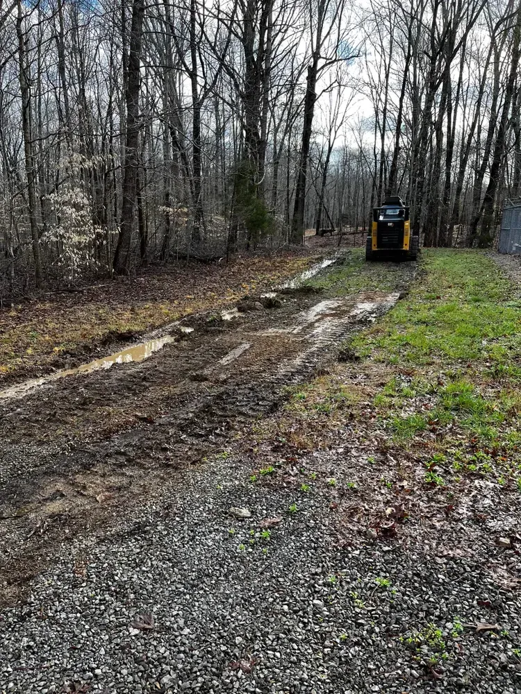 A bulldozer is driving down a dirt road in the woods.