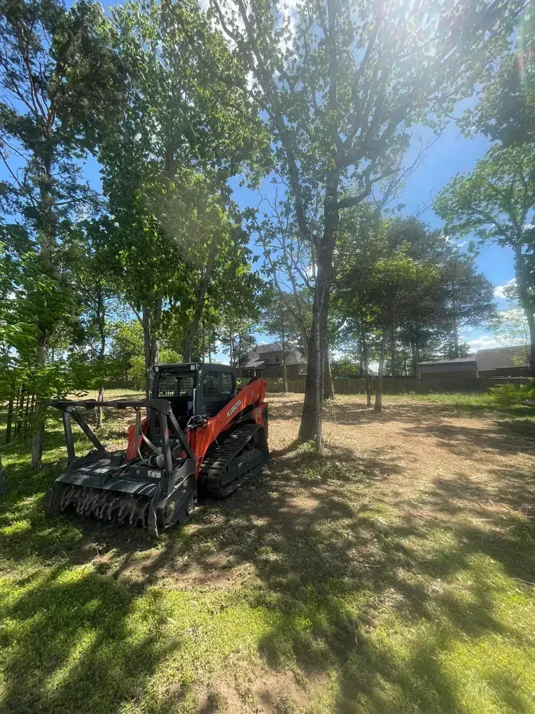 A small tractor is parked in a grassy field surrounded by trees.