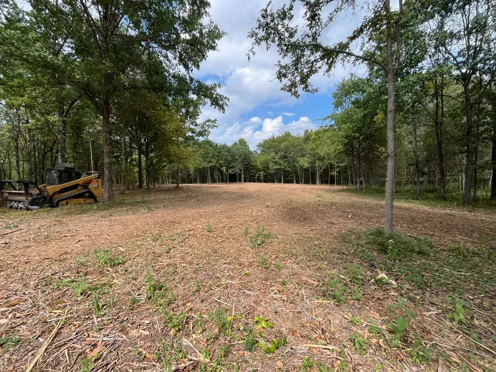 A tractor is parked in the middle of a field surrounded by trees.
