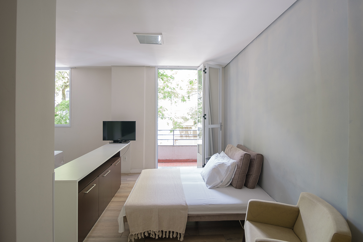 Um quarto com cama, sofá, televisão e varanda.