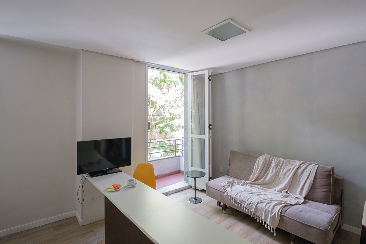 Uma sala com sofá, mesa, televisão e varanda.