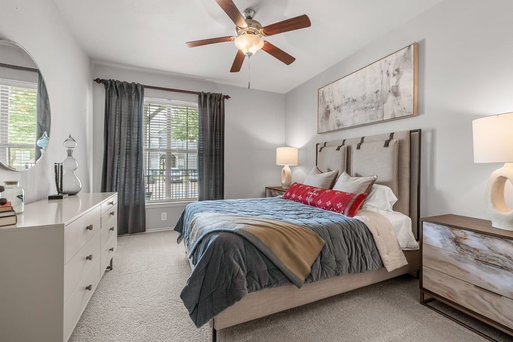 a bedroom with a bed, dresser, mirror, and ceiling fan at Marquis at Lantana in Flower Mound, TX.