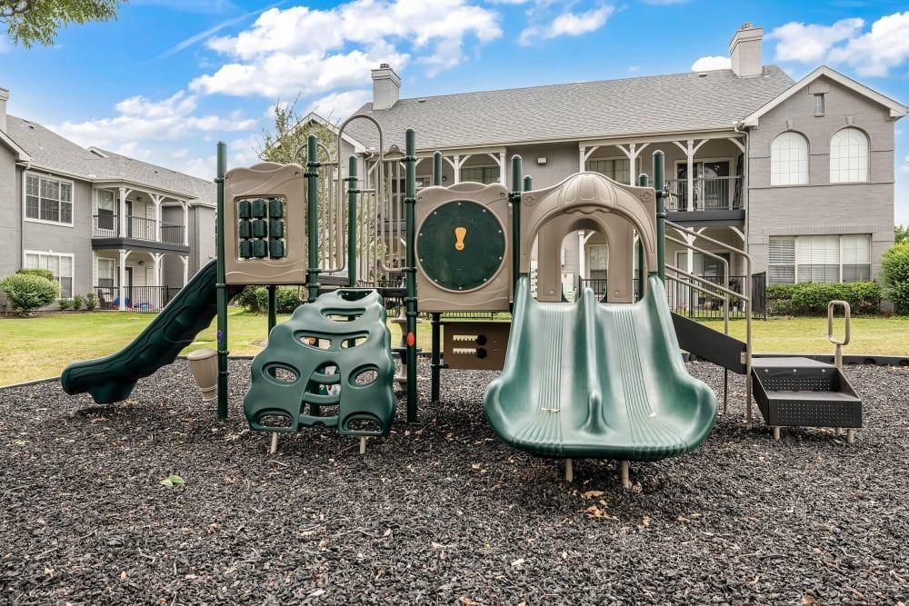 a playground in front of a building with a slide at Marquis at Lantana in Flower Mound, TX.
