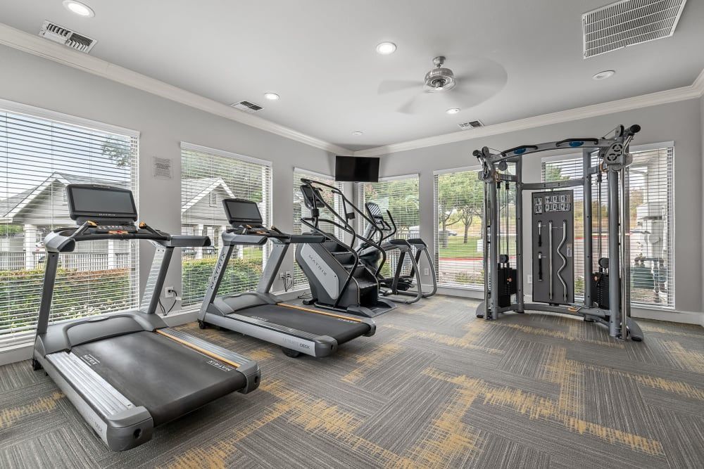 a gym with treadmills, exercise bikes, and a ceiling fan at Marquis at Lantana in Flower Mound, TX.