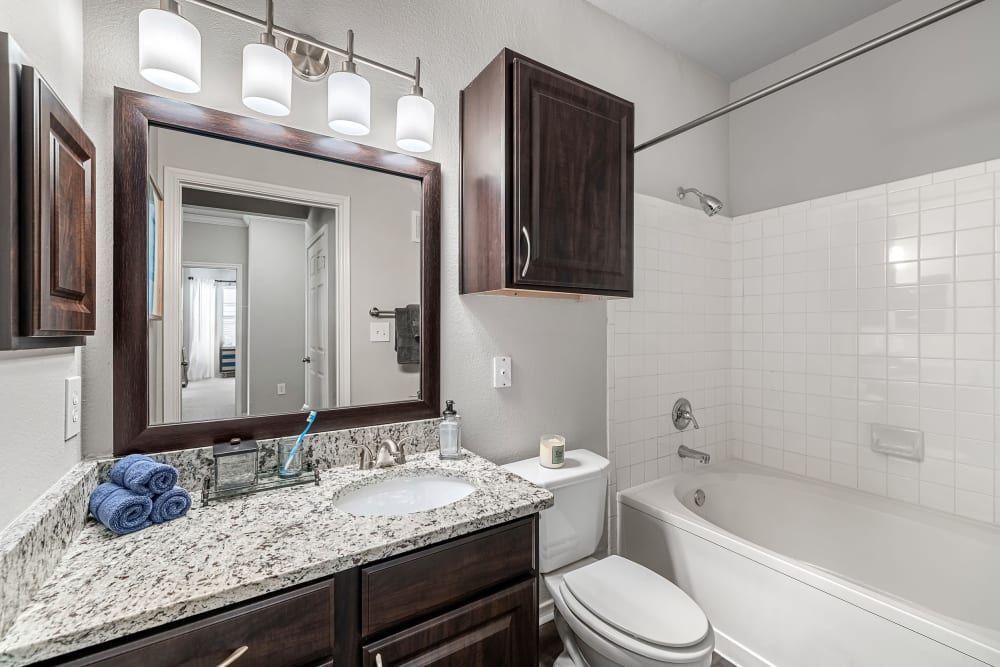 a bathroom with a sink, toilet, tub, and mirror at Marquis at Lantana in Flower Mound, TX.