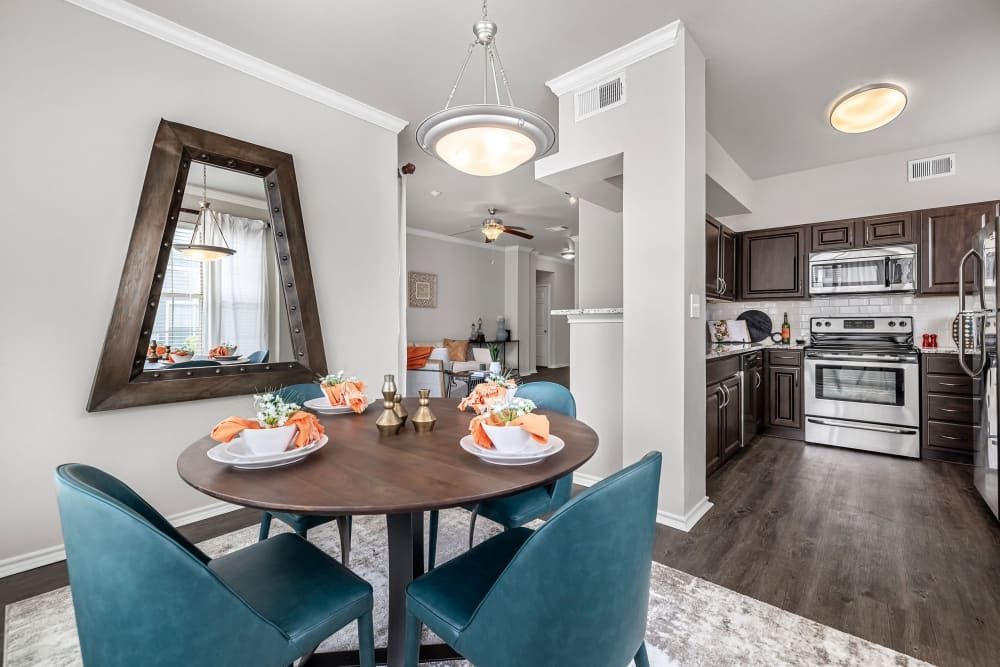 a dining room with a round table and blue chairs and a kitchen in the background at Marquis at Lantana in Flower Mound, TX.