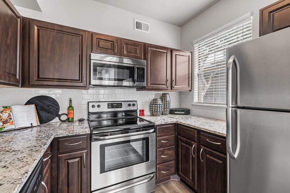 a kitchen with stainless steel appliances, granite counter tops, and wooden cabinets at Marquis at Lantana in Flower Mound, TX.
