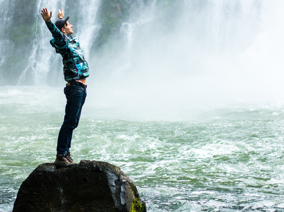 Man standing at the bottom of a waterfall with hands in the air
