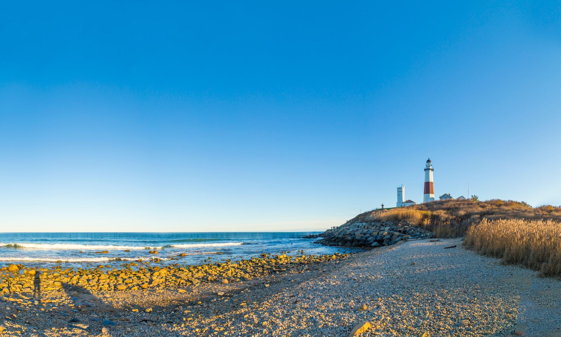 Montauk Point Lighthouse on rocky shore with blue sky and ocean.