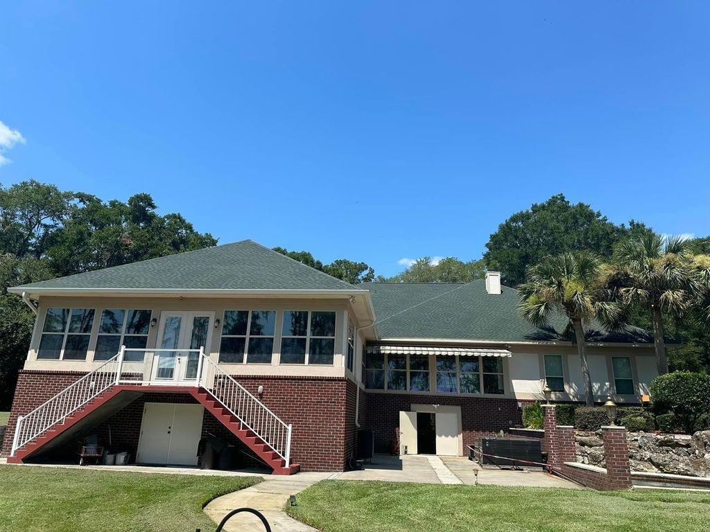 Explore this spacious suburban home design featuring a prominent glass sunroom, brick accents, and a wide backyard view. A perfect example of functional, multi-level outdoor access and coastal-inspired architecture.