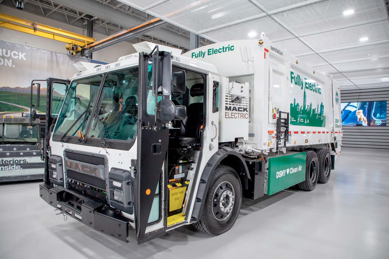 A white and green garbage truck is parked in a building.