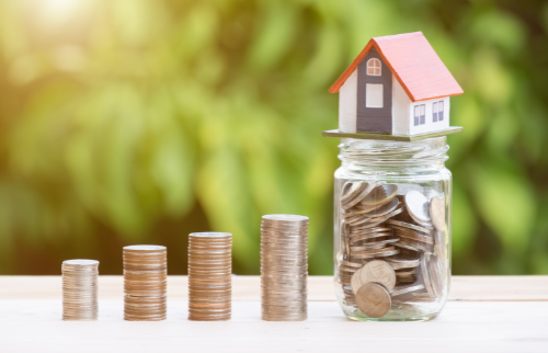 Photo of a toy house sitting on a jar of coins.