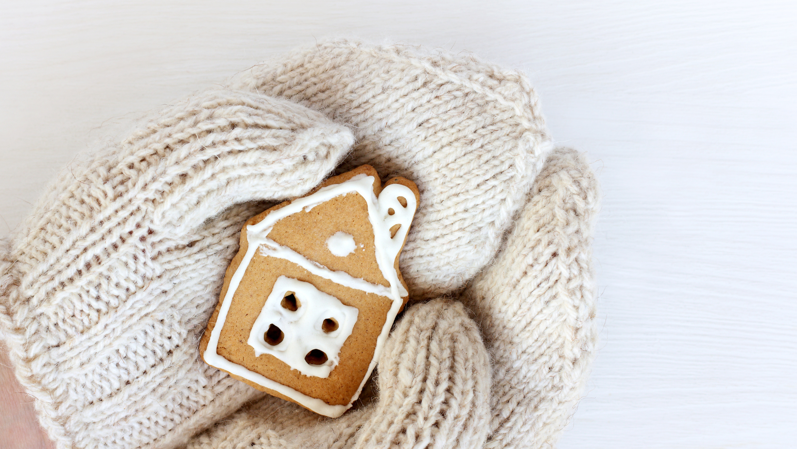 Hands in knitted mittens holding a gingerbread house.