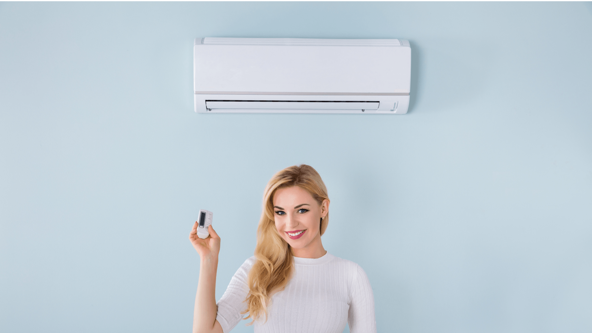 Picture of a women standing in front of a ductless unit with a remote control.