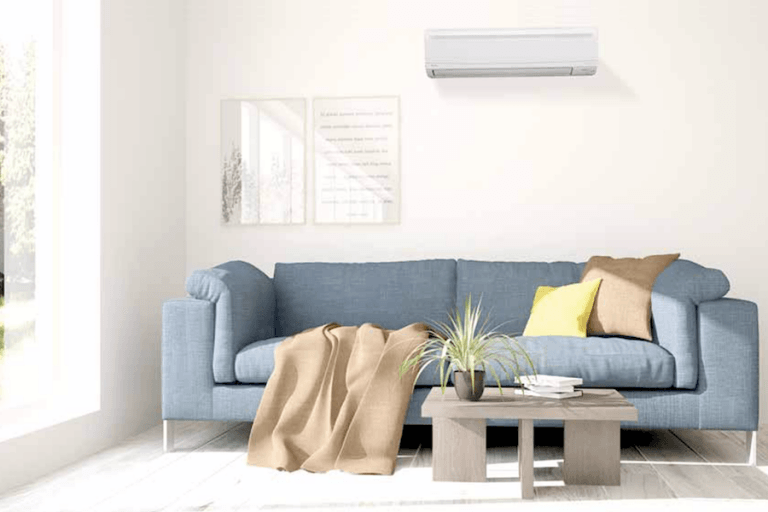 Photo of a dark blue colored couch infront of a small coffee table. An inverter type of aircon is installed on top of the wall behind it.