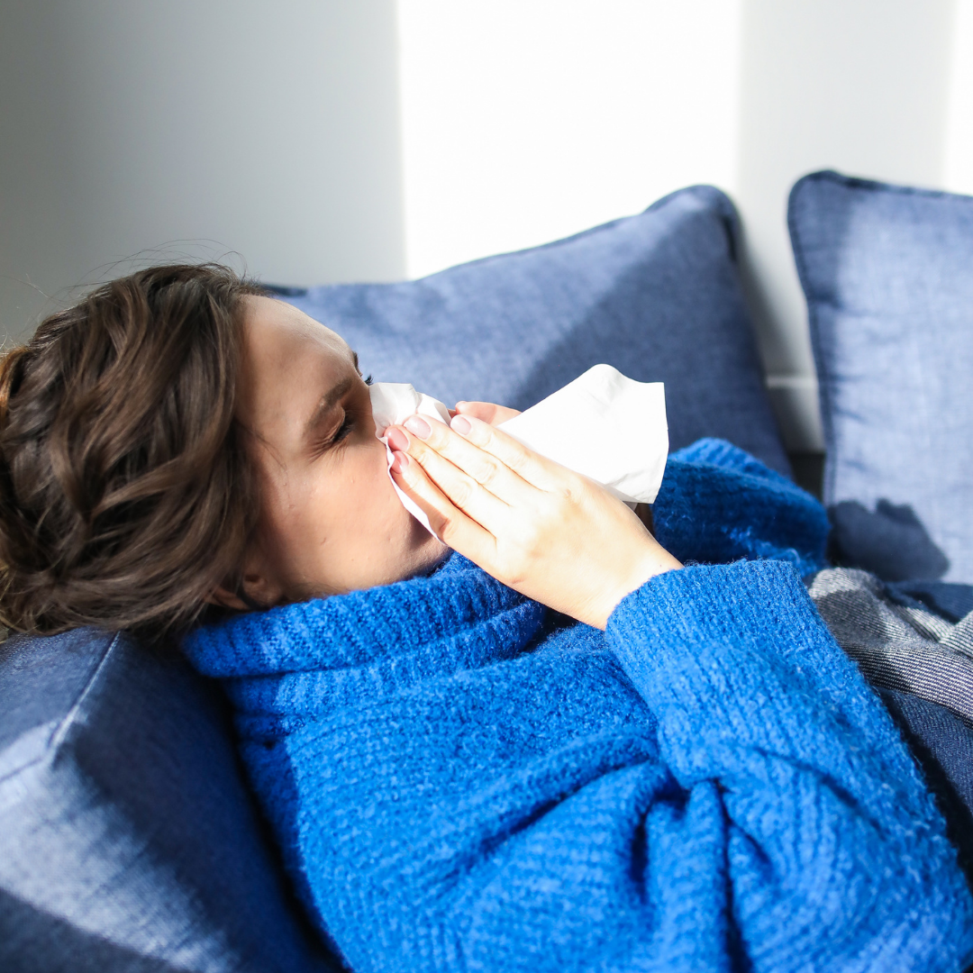 Picture of a woman laying on her couch blowing her nose.