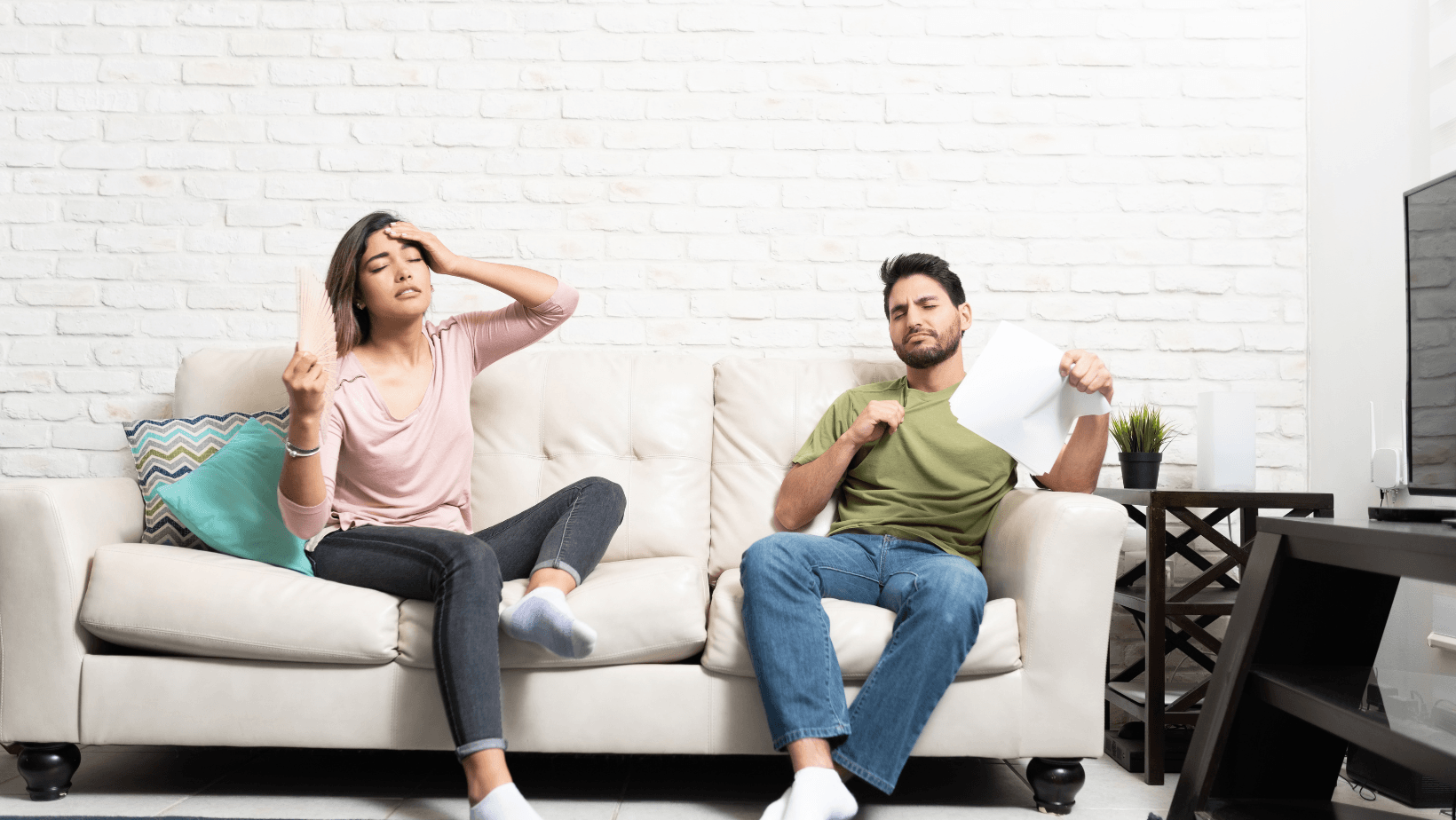 Picture of a woman and a man sitting on a couch feeling too hot.