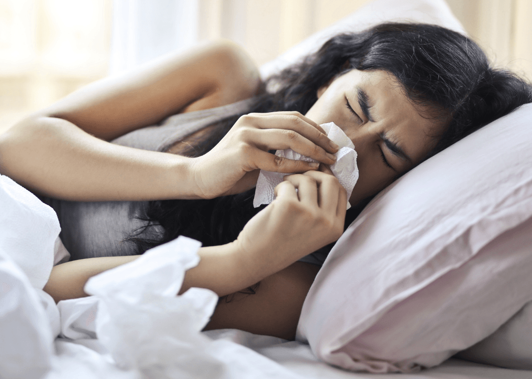 Image of a woman laying in bed blowing her nose.