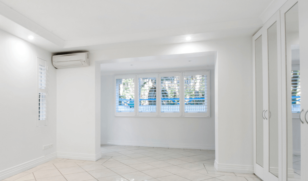 Picture of an empty room with a ductless heat pump unit in the corner.