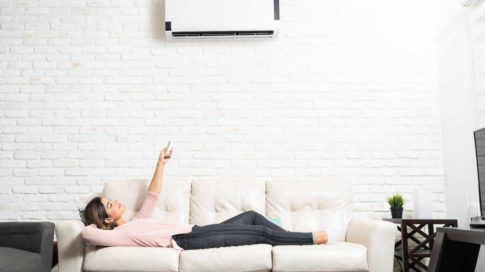 woman lying in the couch turning on the mini split AC unit