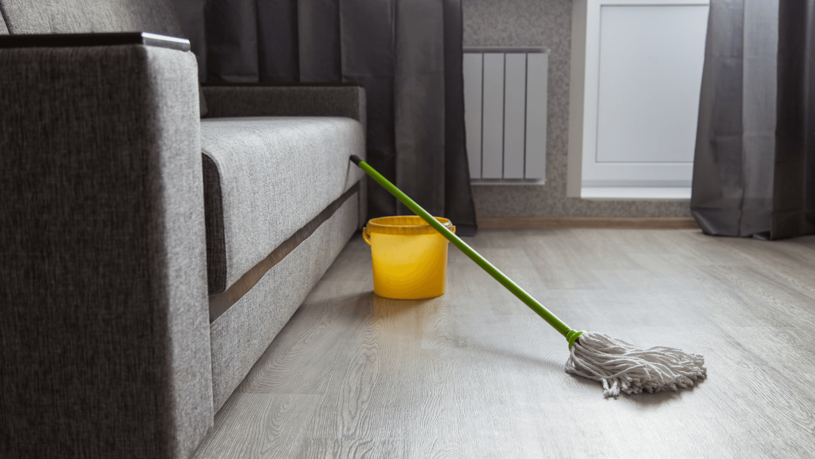 Picture of a mop and bucket leaning up against a couch.