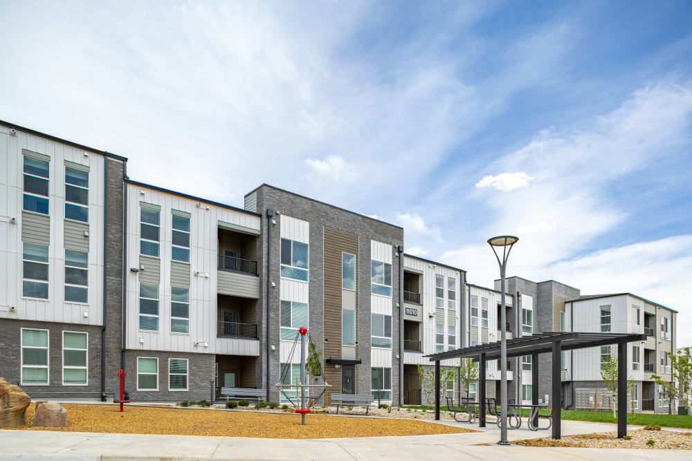 Modern apartment complex featuring gray and white buildings with balconies, a covered bus stop in the foreground, and a blue sky with light cloud cover in the background at Marq Perimeter in Atlanta, GA.