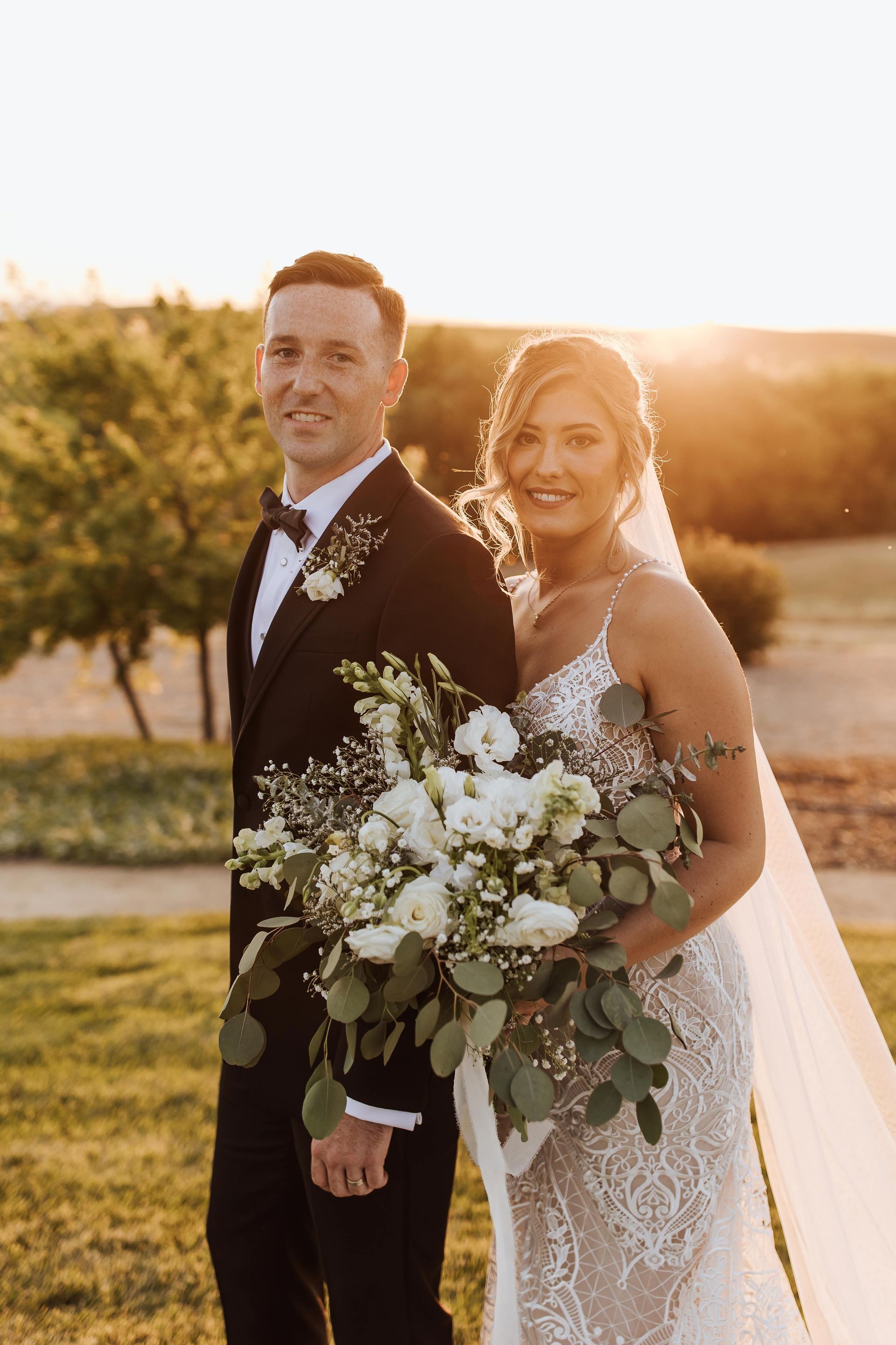 a bride and groom pose for a picture with a bouquet of white flowers