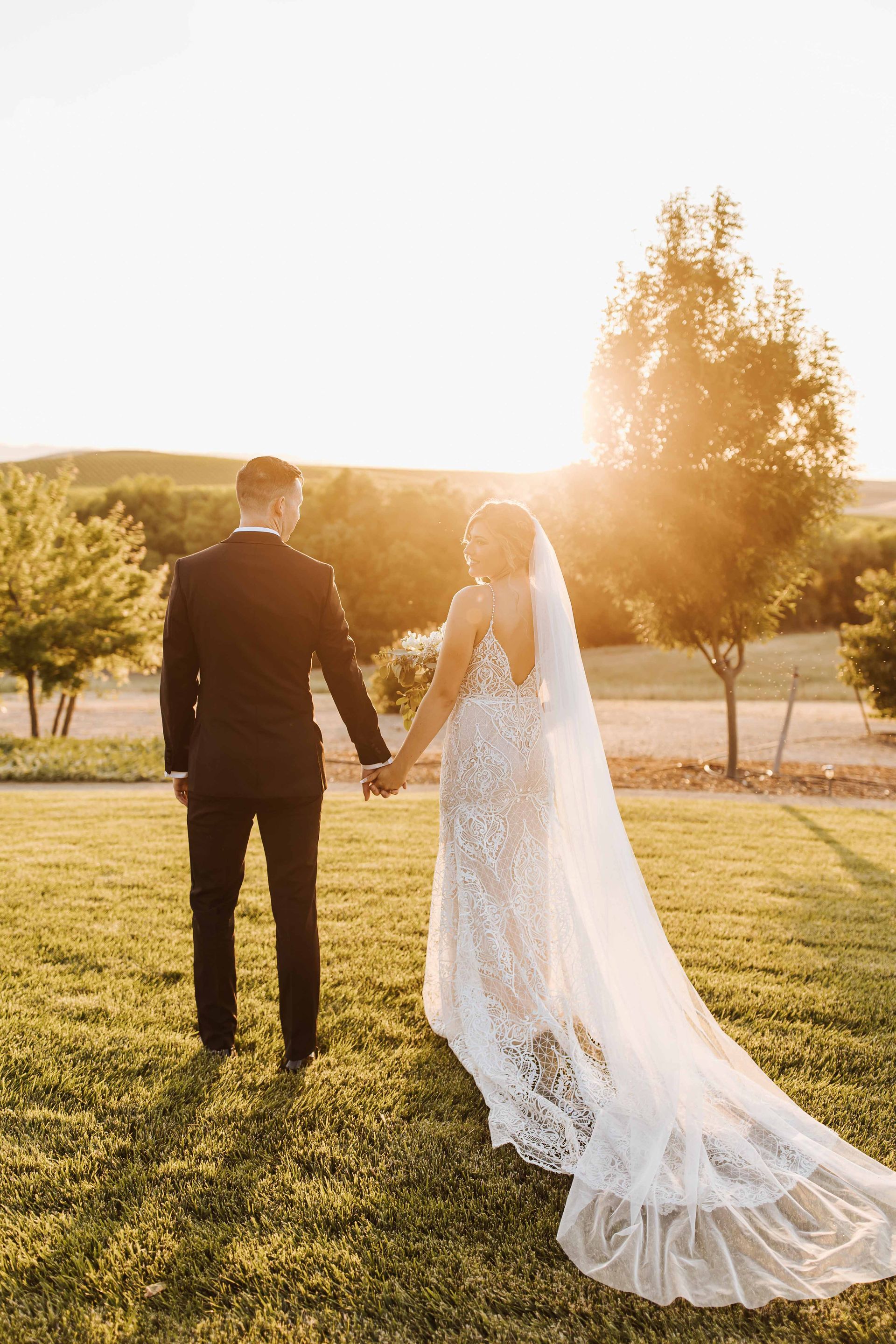 a bride and groom hold hands as the sun sets behind them