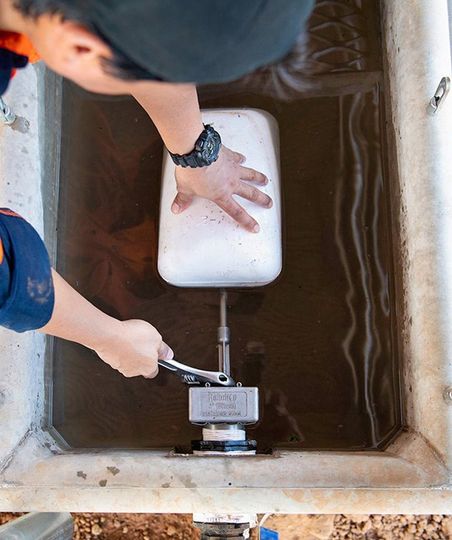 A person is installing a water trough float system with a wrench.
