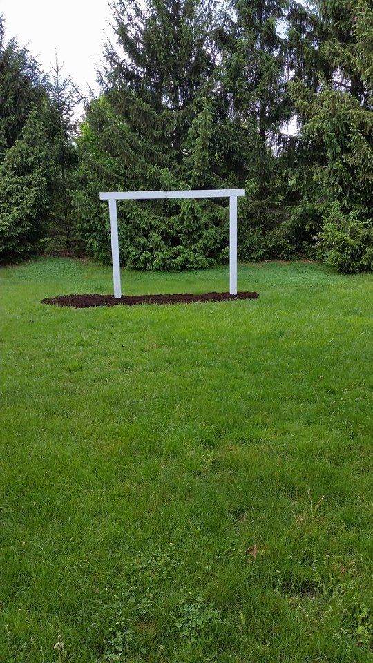 A white soccer goal is in the middle of a lush green field.