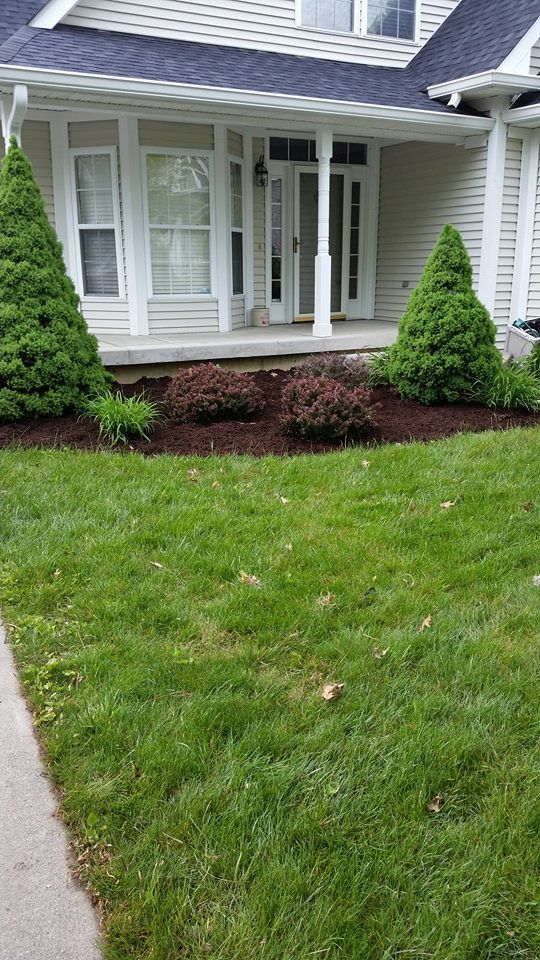 A lush green lawn in front of a house with a porch.