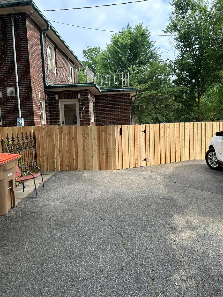 A car is parked in front of a wooden fence in front of a brick house.