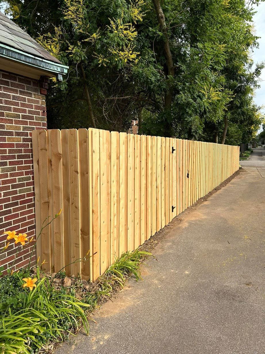 A wooden fence is sitting on the side of a road next to a brick building.