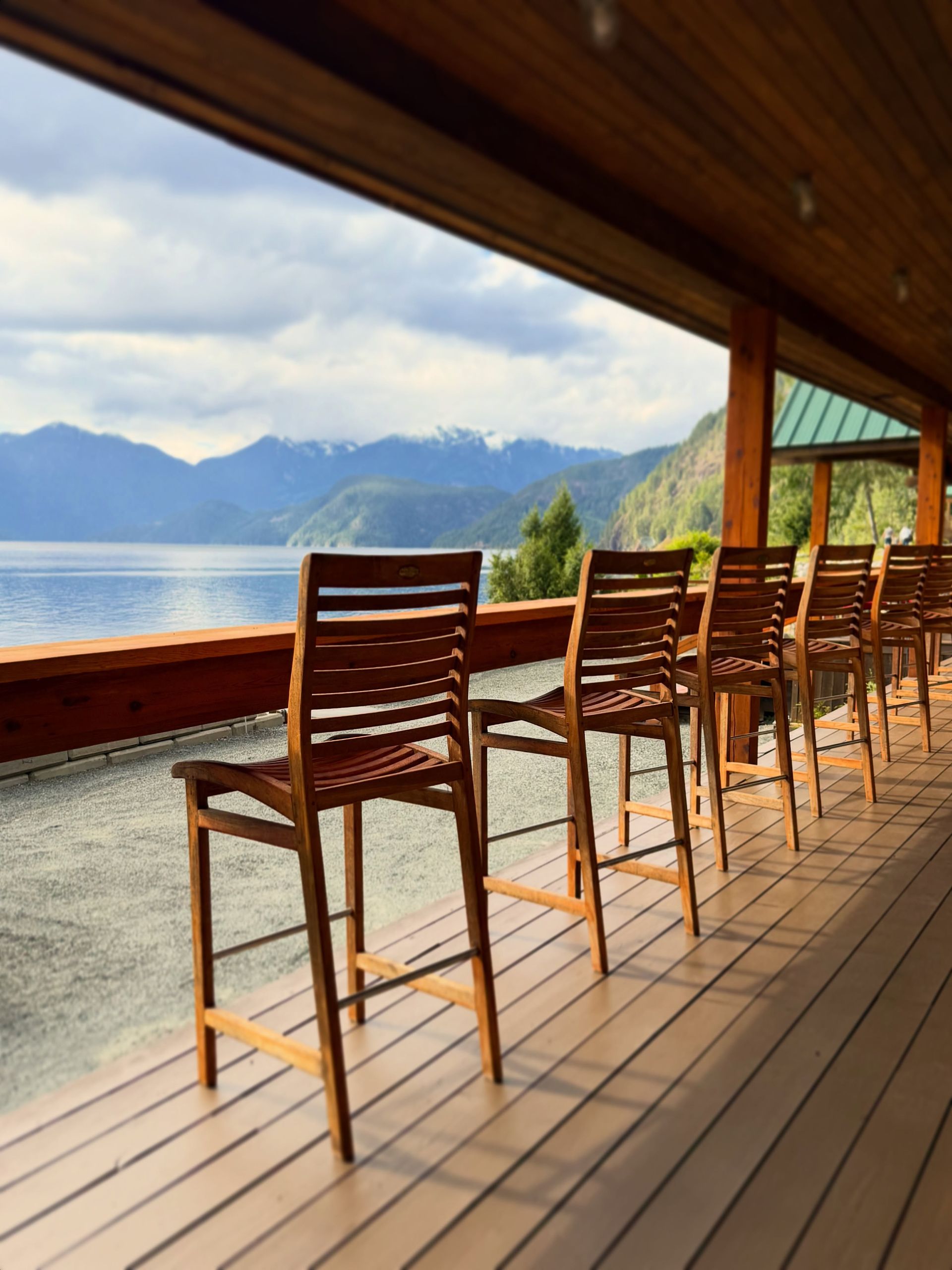 Houten stoelen op een terras aan het meer met uitzicht op de bergen en het kalme water.