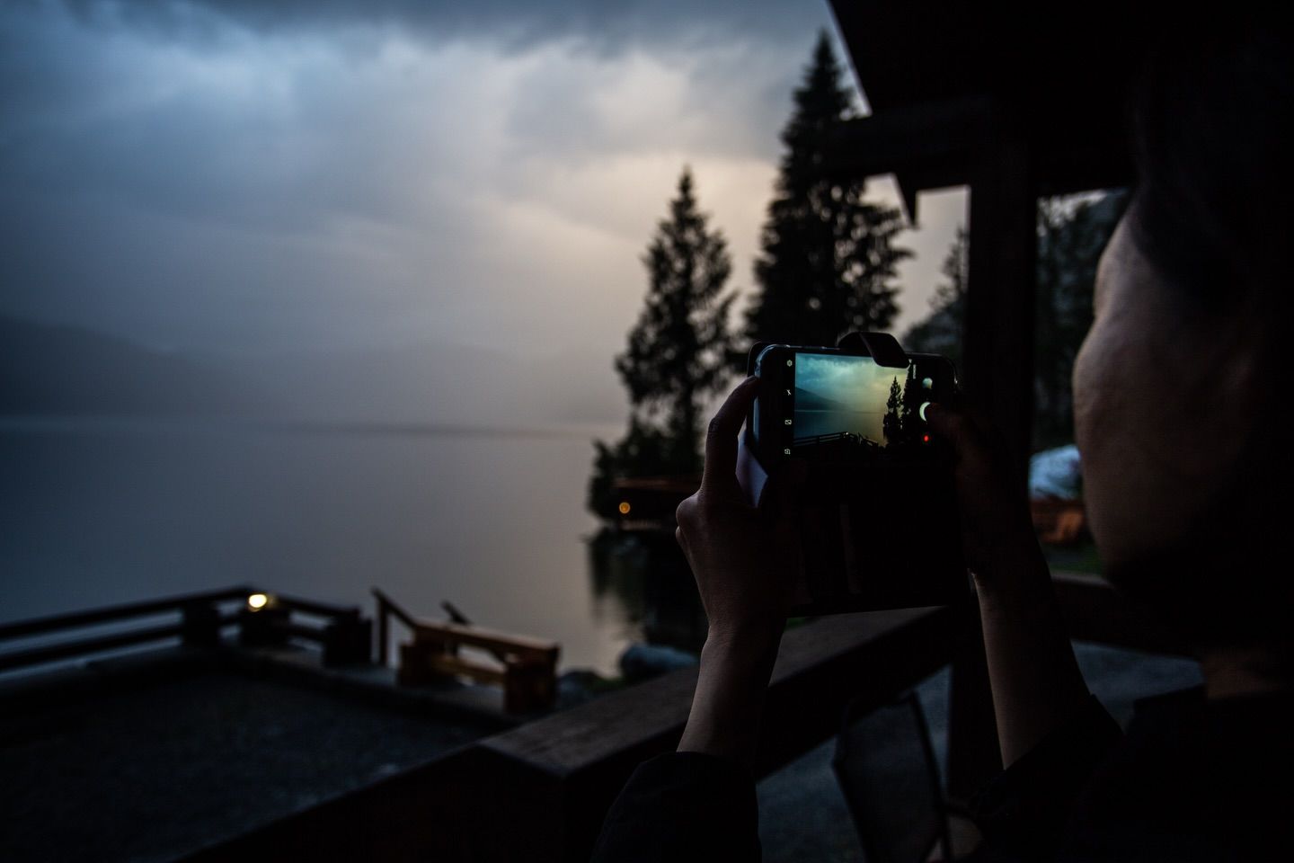 Iemand fotografeert vanaf een veranda een donkere, stormachtige lucht boven een meer in de schemering.