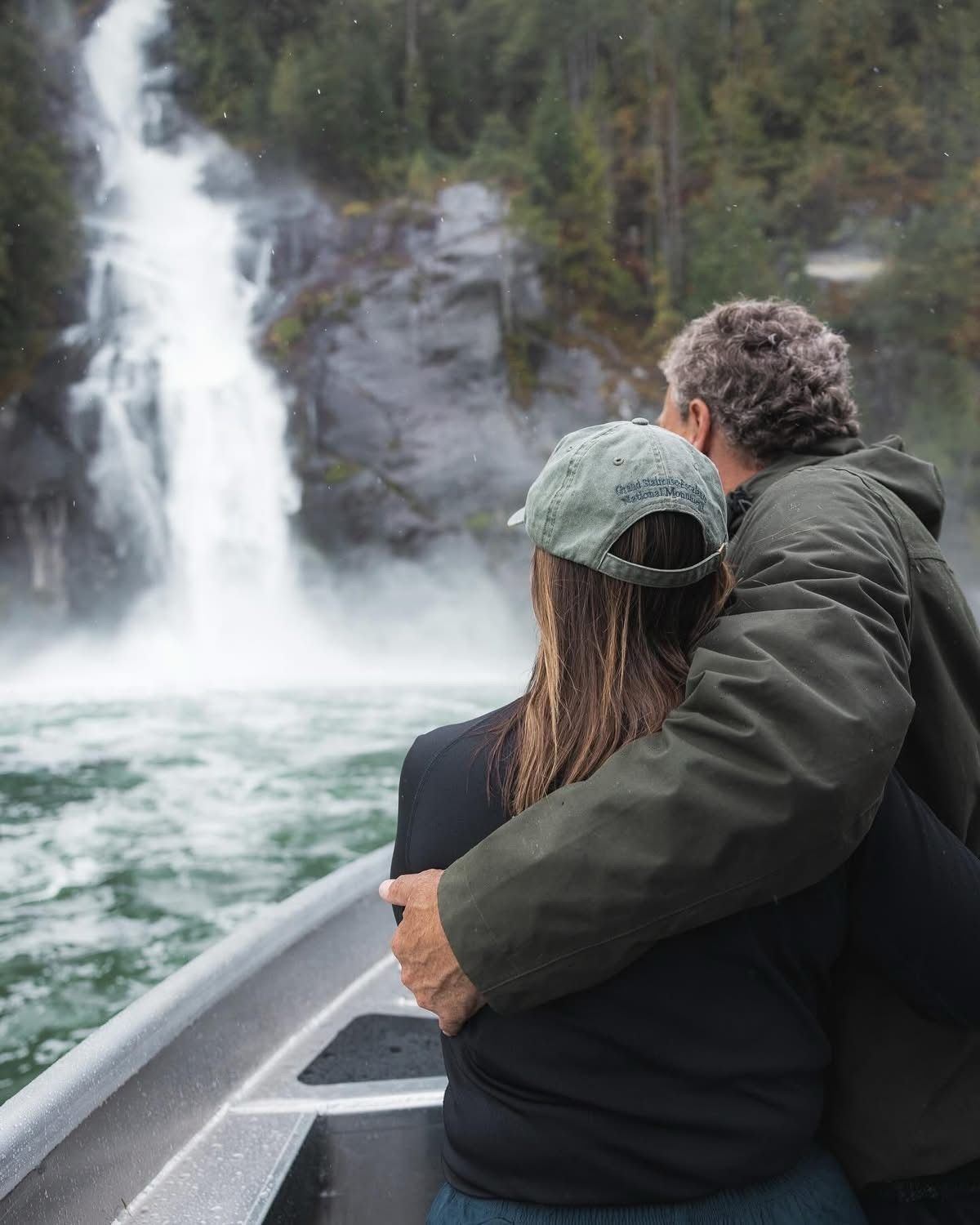 Een stel in een boot kijkt naar een hoge waterval in een beboste kloof.