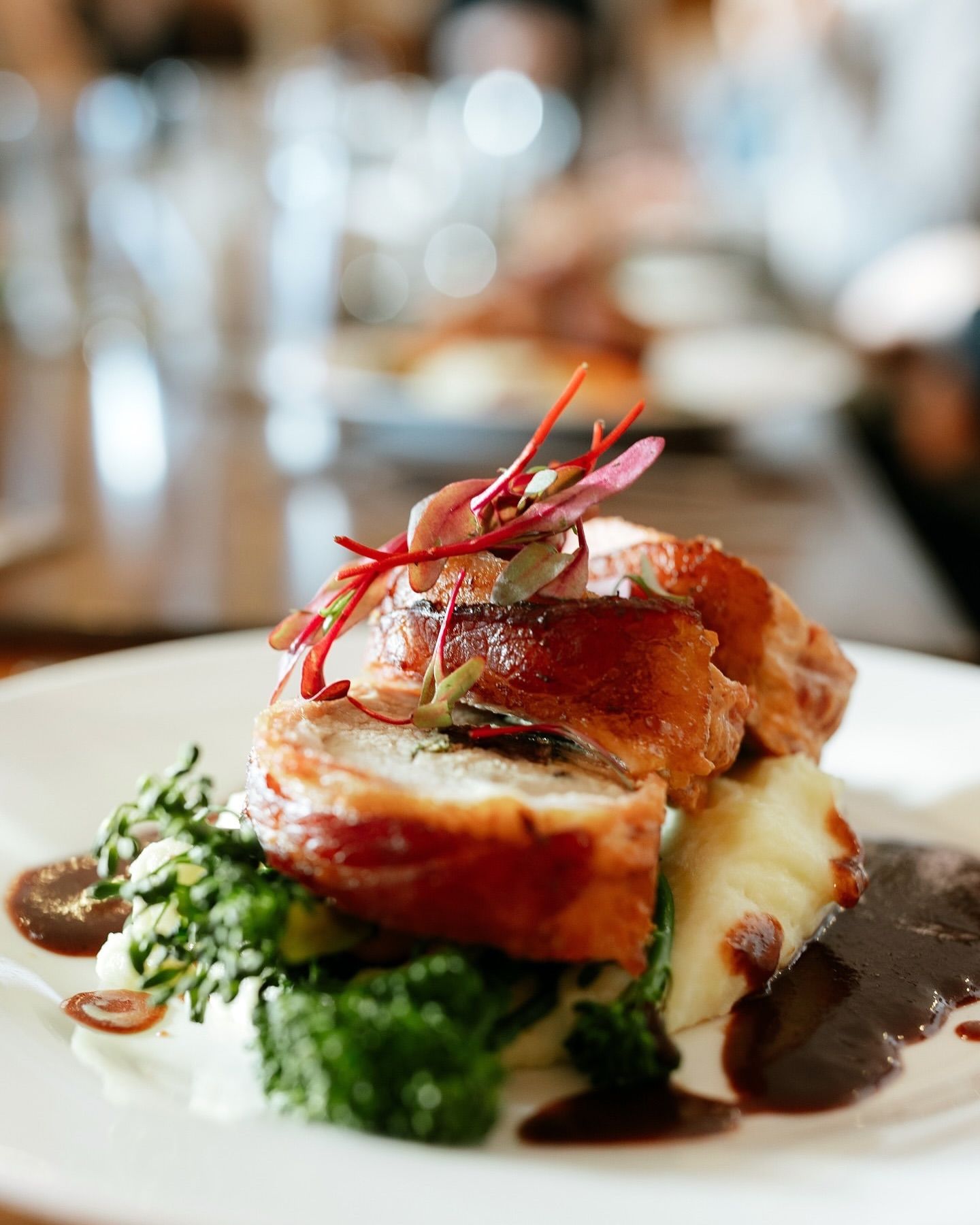 Een gastronomisch gepresenteerd vleesgerecht met groenten en een rijke saus, geserveerd op een wit bord in een restaurantomgeving.