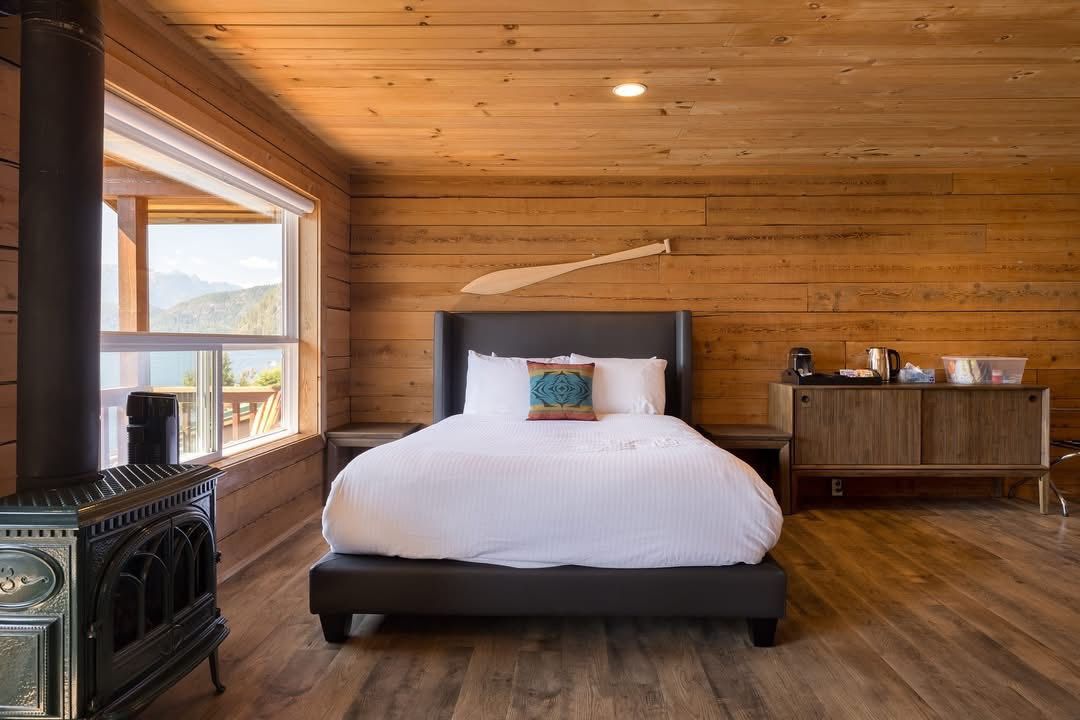Gezellige slaapkamer met houten lambrisering, een bed, uitzicht door het raam, een antieke kachel en een commode.