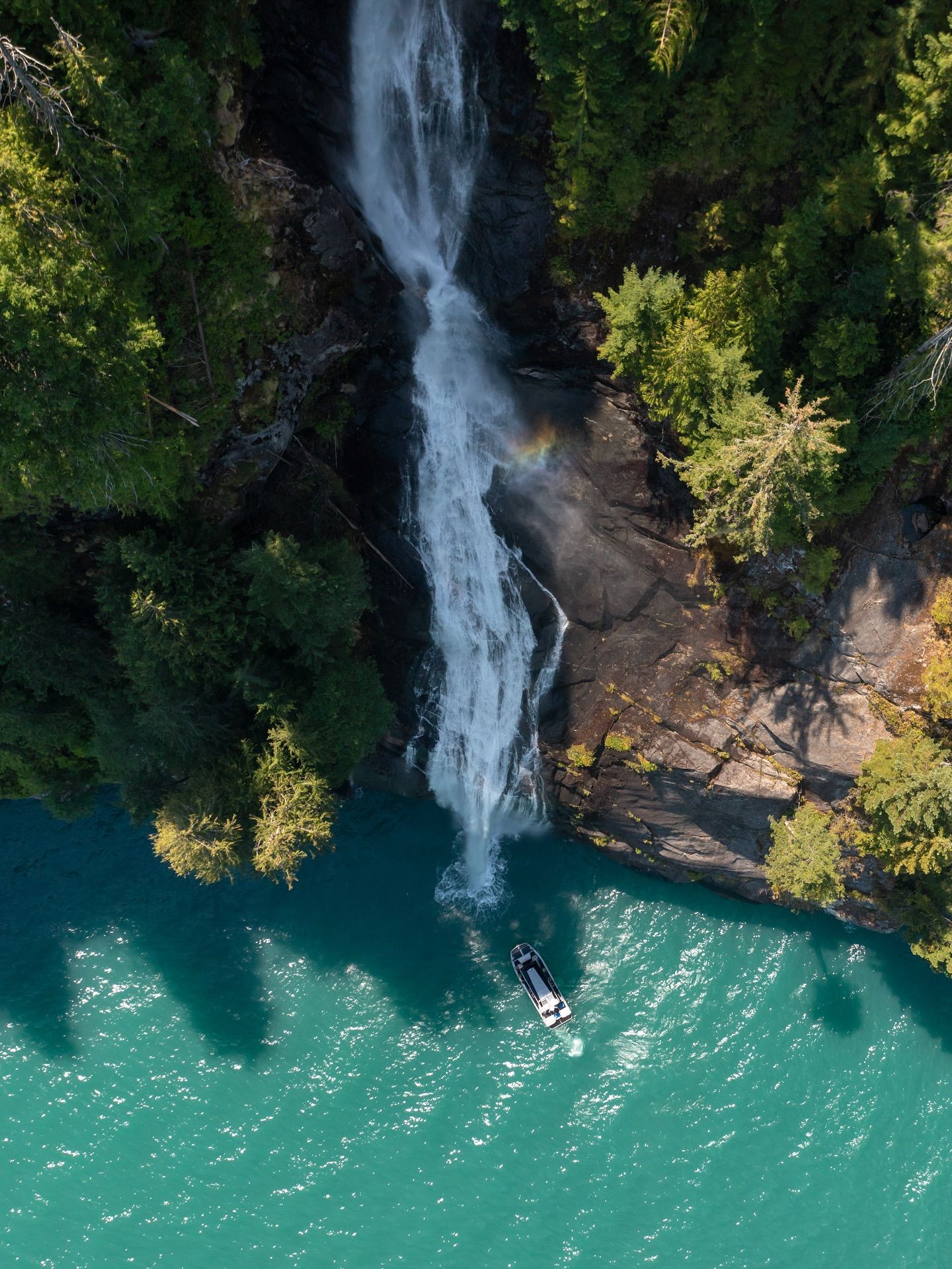 Luchtfoto van een waterval die in turquoise water stort, naast rotsachtige kliffen en dichte groene bomen.