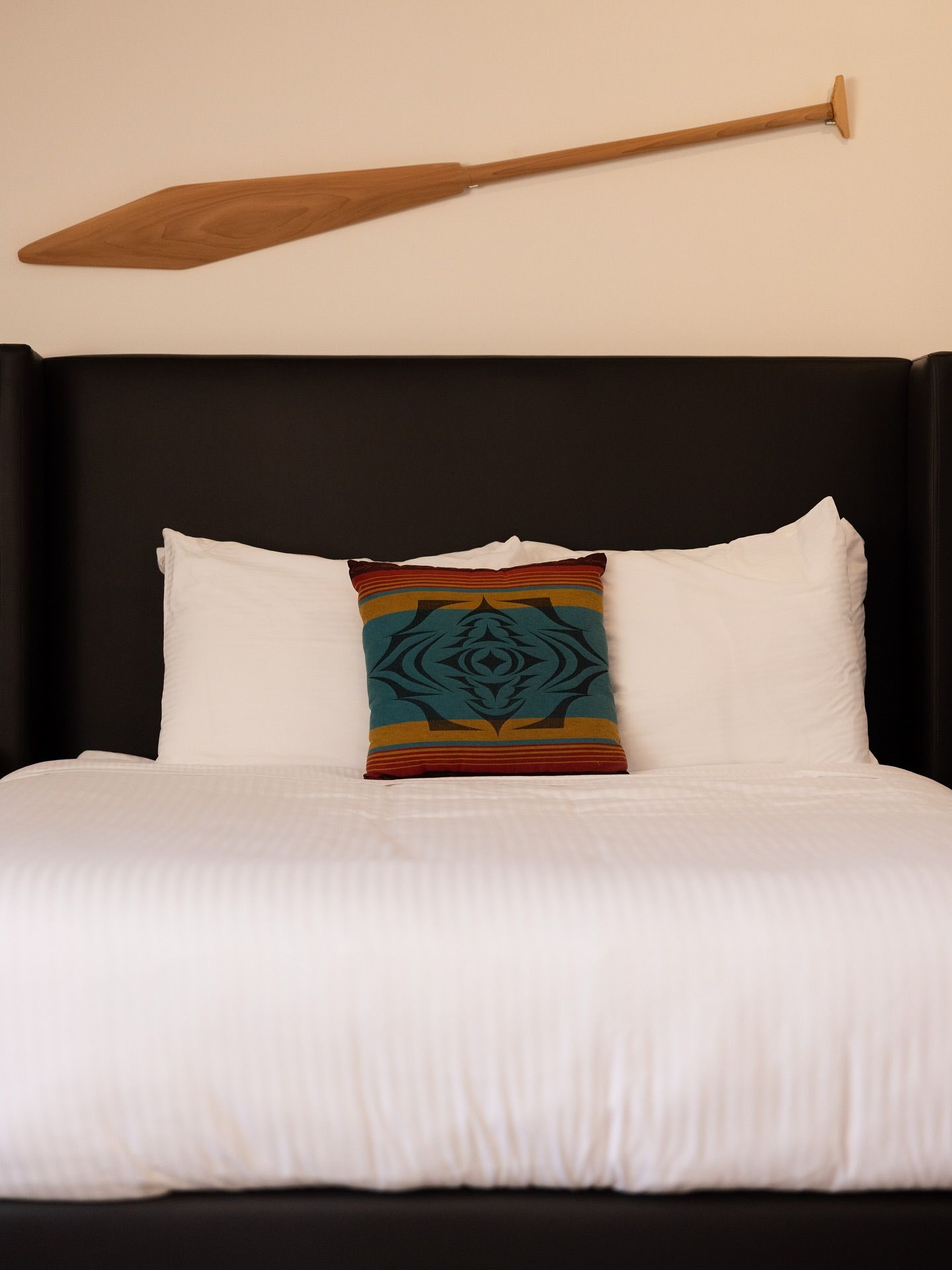 Netjes opgemaakt bed met wit beddengoed, zwart hoofdeinde en een decoratieve peddel erboven.
