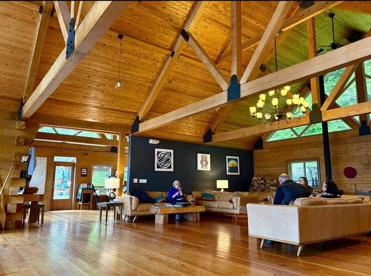 Ruime, houten lounge met gewelfd plafond, banken, tafels en een persoon die aan een centraal bureau zit.