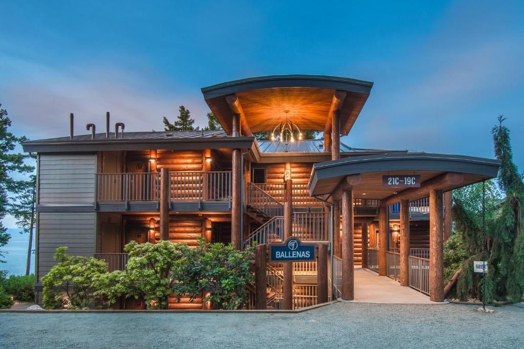 Houten lodge met warm licht in de schemering, omgeven door groen en een blauwe hemel.