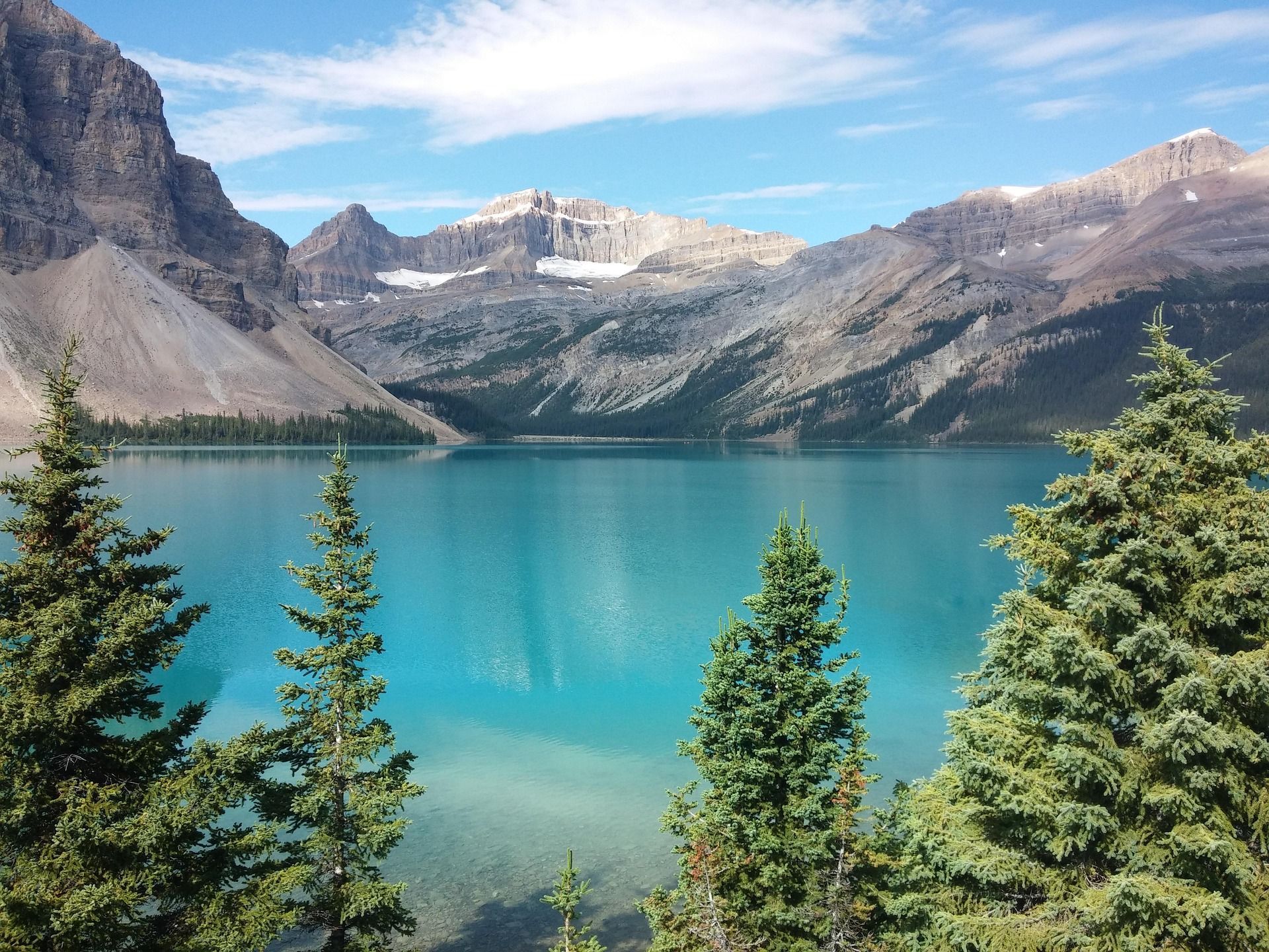 Turquoise lake with mountains in the background, evergreen trees frame the view under a blue sky.