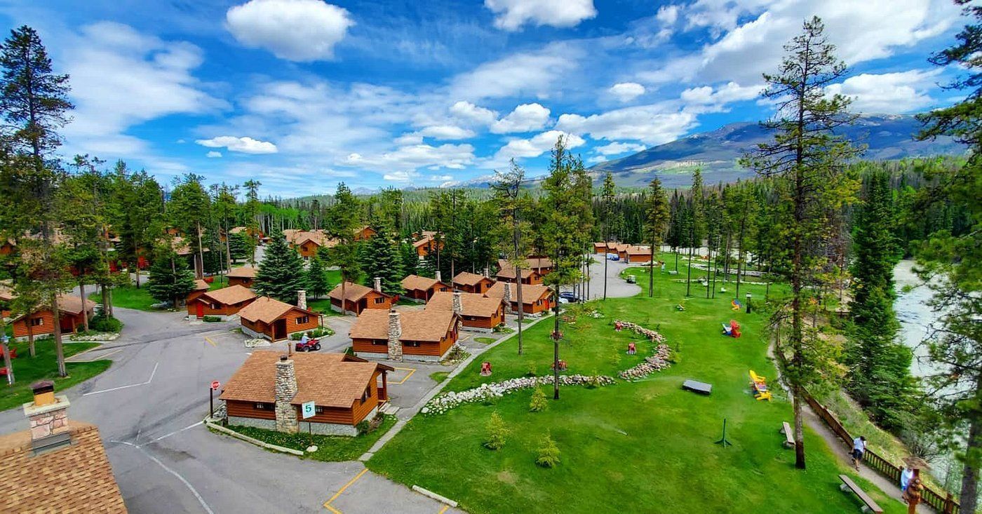 Luchtfoto van Becker's Chalets Jasper met hutten met oranje daken, groene gazons en bomen onder een blauwe hemel.
