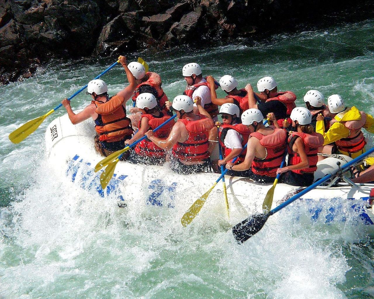 People rafting in a white water rapid, paddling in unison.