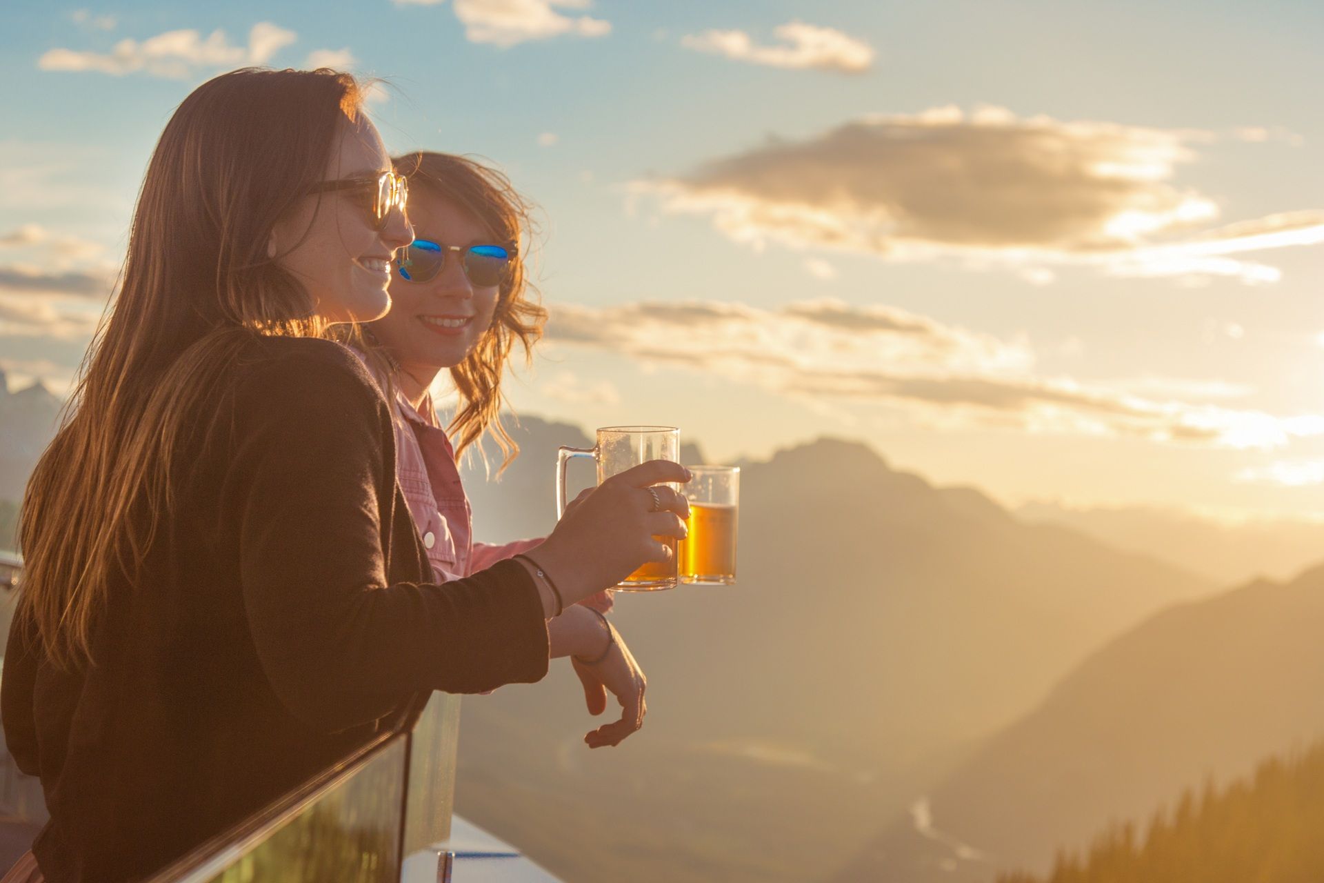 Twee mensen brengen een toast uit met drankjes op een balkon met uitzicht op de bergen bij zonsondergang.