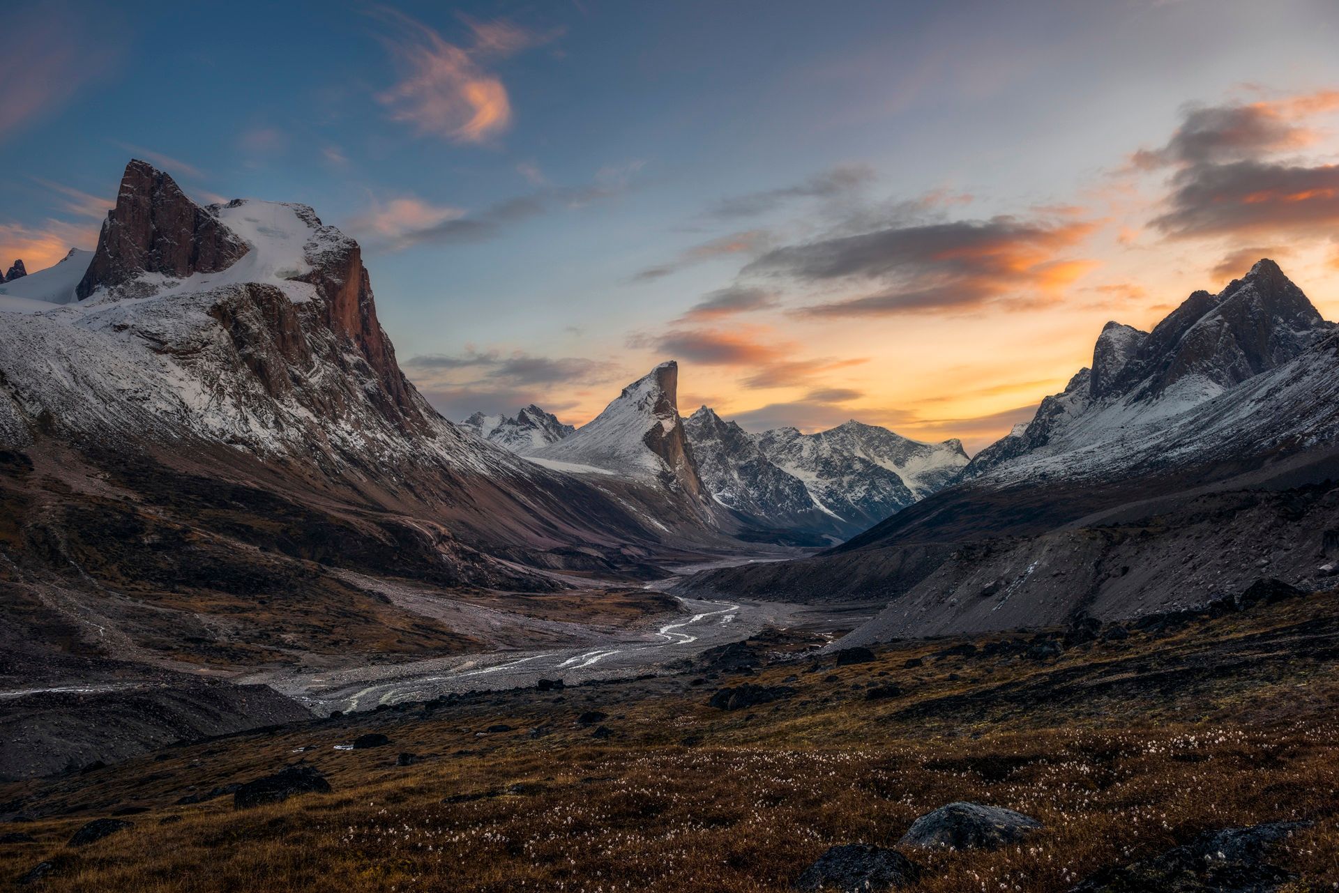 Snow-capped mountains at sunset with a valley and golden sky.