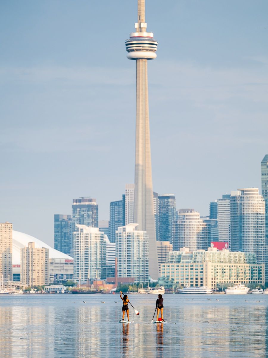 Credits KBialous Two people paddleboard on water, CN Tower and Toronto skyline in background.